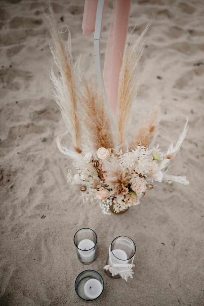 Hochzeitsdeko mit Blumen, Kerzen und Pampasgras am Strand.