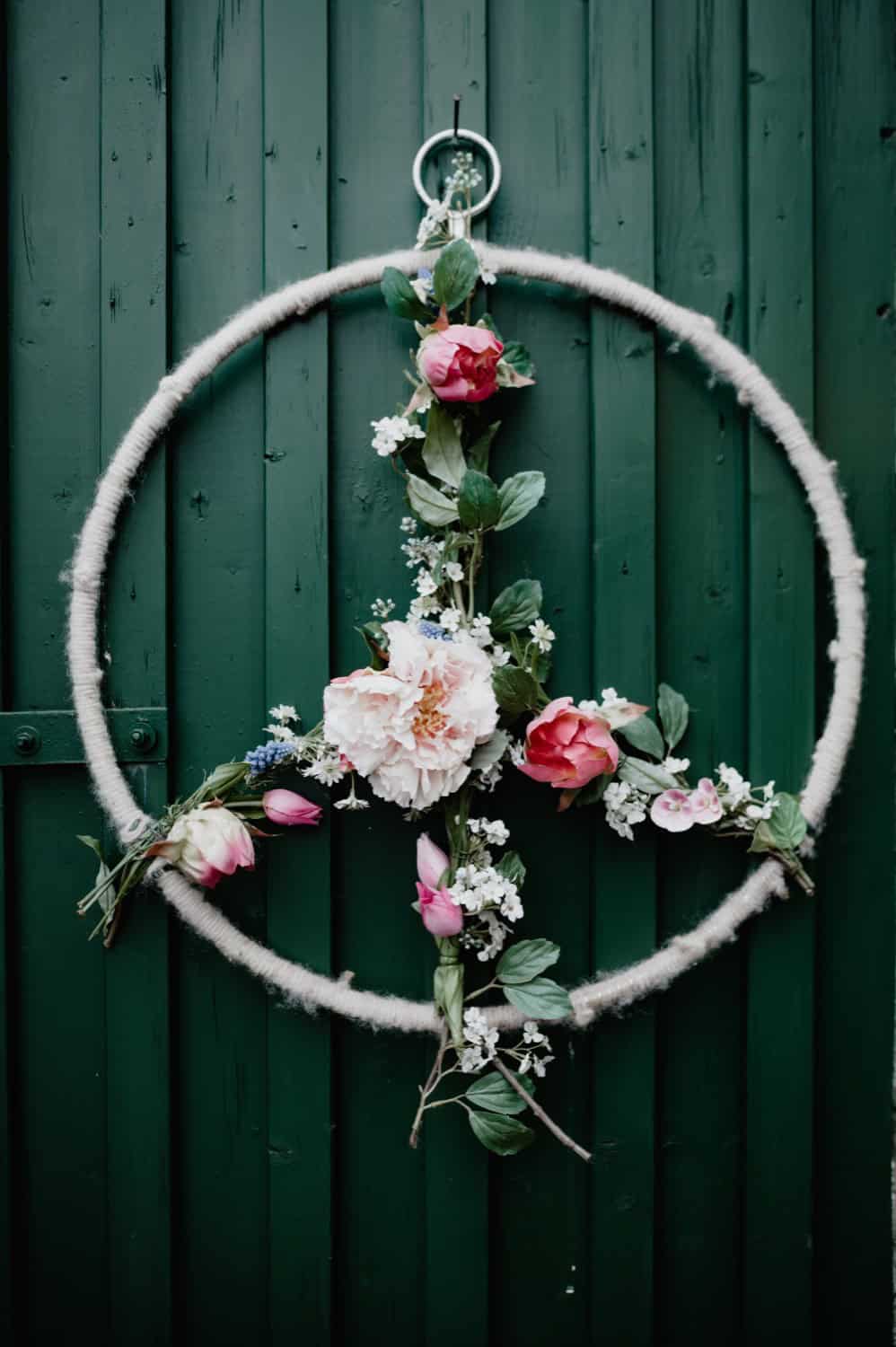 Blumenkranz mit Rosen und Blüten an grüner Holztür.